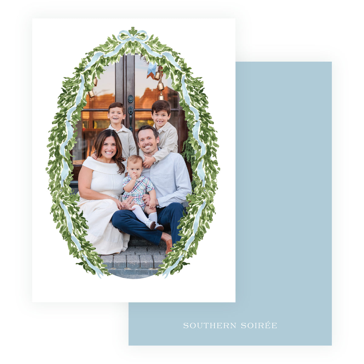 A white greeting card with a family photo framed in an oval green leaf wreath border, shown with a light blue card back.