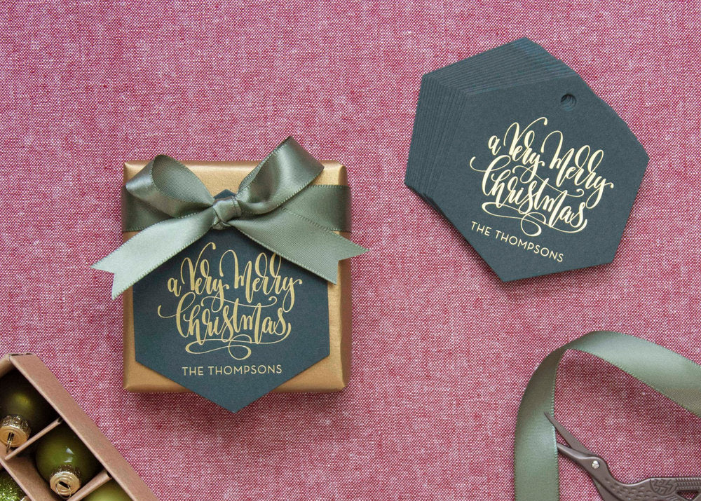 Gift box with green ribbon and personalized 'A Very Merry Christmas' tag on a pink textured background.