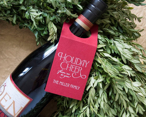 Wine bottle with a 'Holiday Cheer' tag on a green leafy background